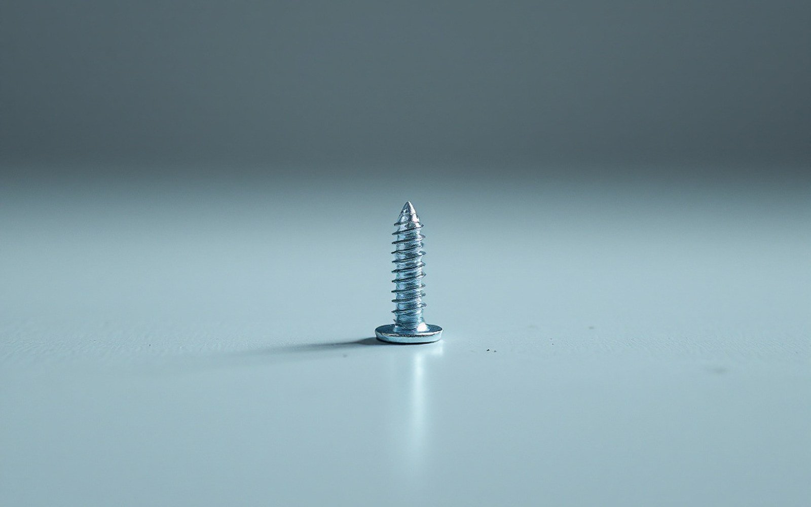 One small screw lying alone on a vast pale floor, shot from standing height